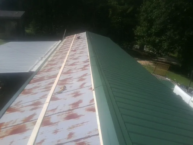 Old rusted panels beside newly installed green metal roofing — Wind Damage Roof Repair by Roofing Brothers in Ligonier