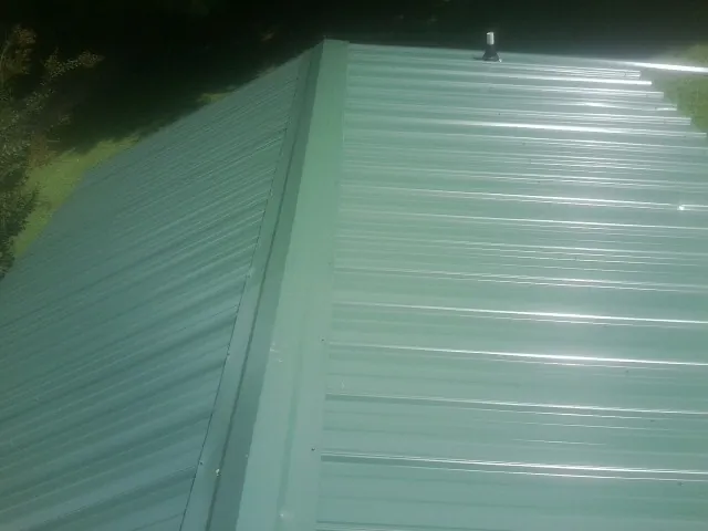 New green metal panels meeting at the ridge of a roof — Flat Roof Repair work by our crew in Ligonier