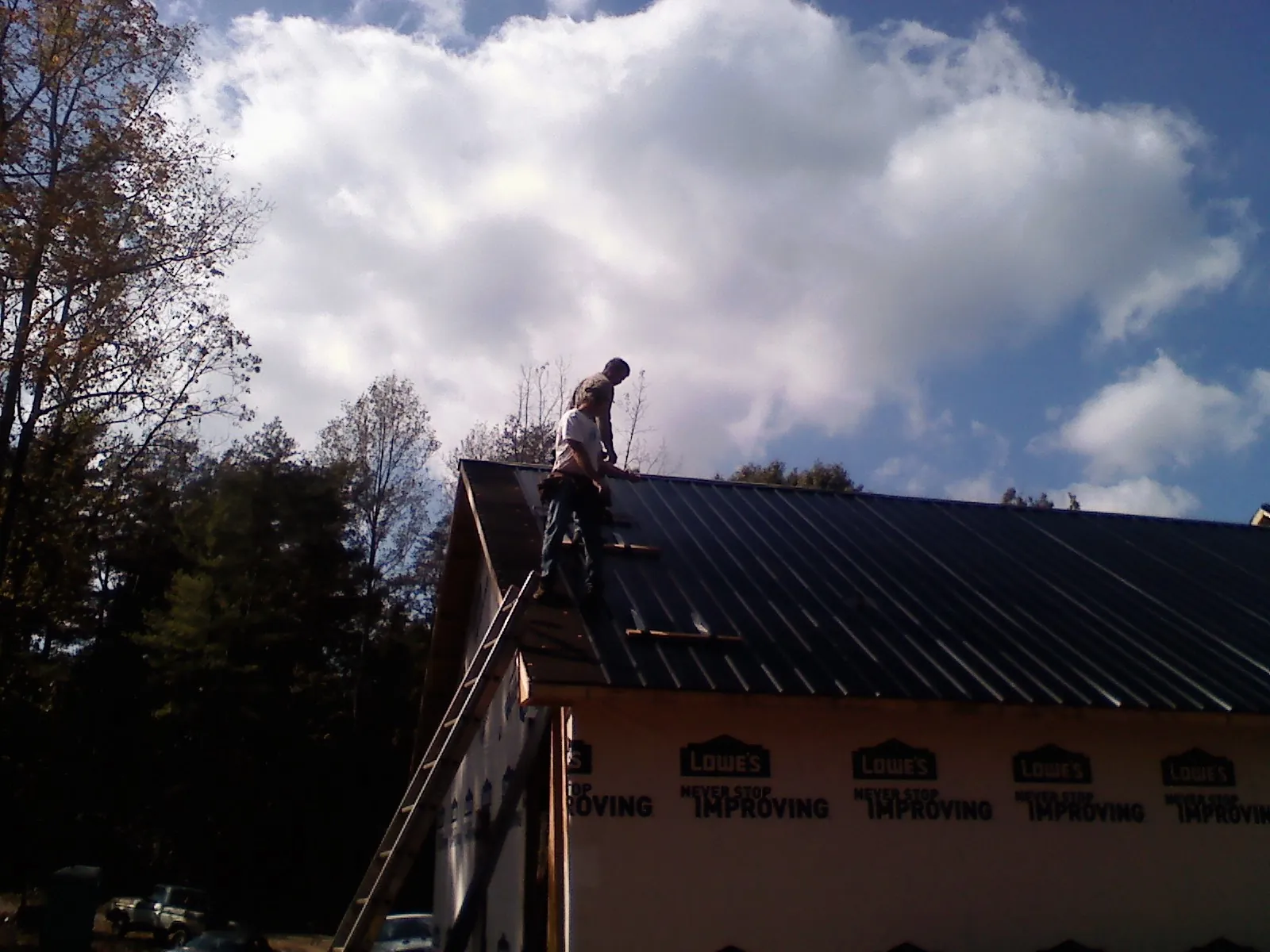 Roofer fastening dark metal panels high against a cloudy sky, from a Roof Inspection job in Ligonier